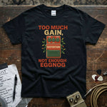 Too Much Gain Not Enough Eggnog Shirt displayed on a black tee surrounded by guitar picks and a music list.