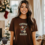 Woman wearing a Torque Queen Shirt in dark chocolate color with a vibrant graphic design, set in a cozy environment.