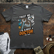 Trust Me I’m Almost a Doctor for Cars | Funny Mechanic T-Shirt in gray featuring a muscular arm and tools.